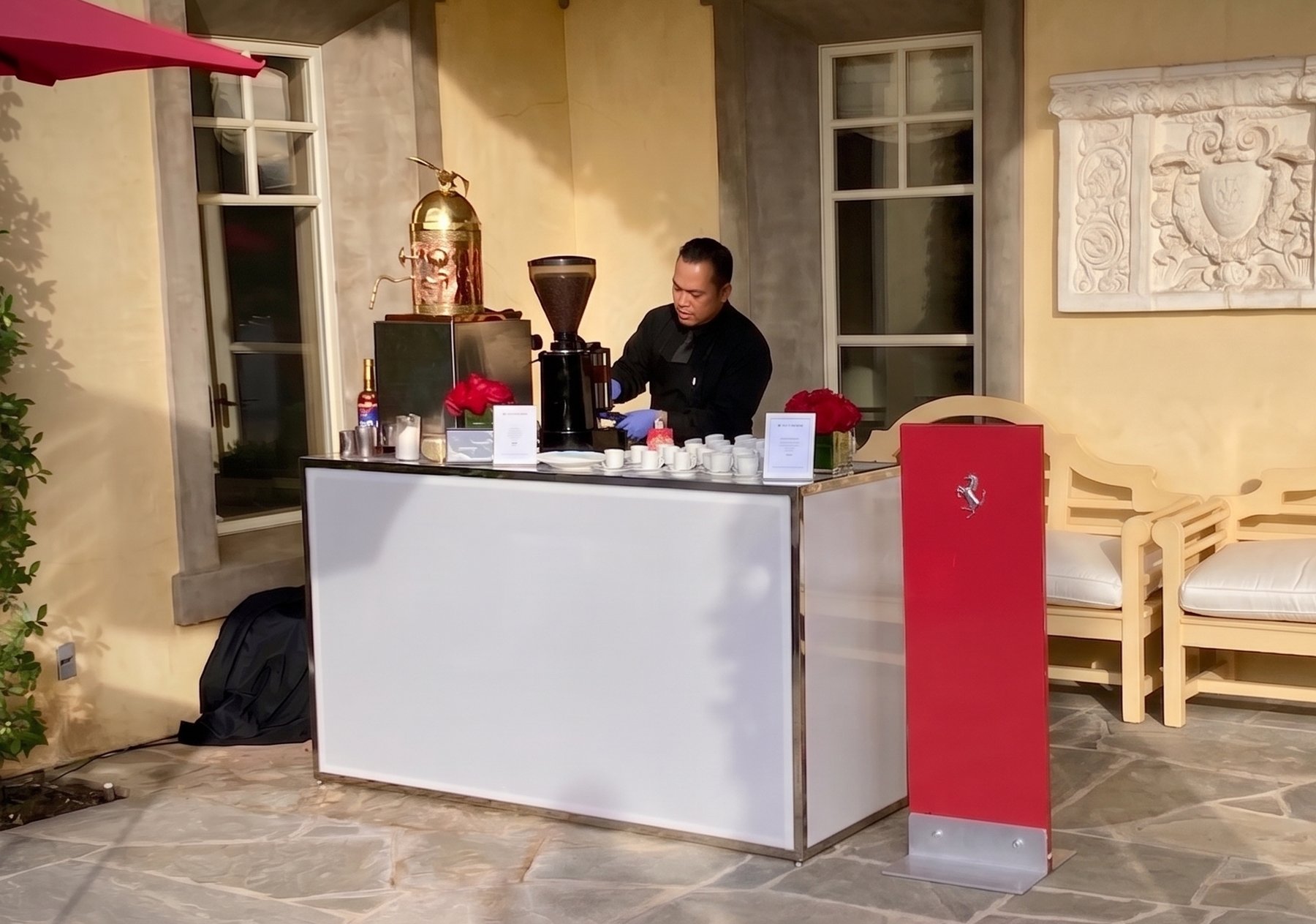 An Espresso Subito barista making drinks at the white event bar with The Dome, at a private Ferrari event